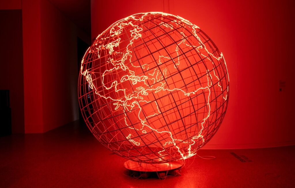A striking illuminated globe sculpture displayed in a dimly lit art exhibition in Bonn, Germany.