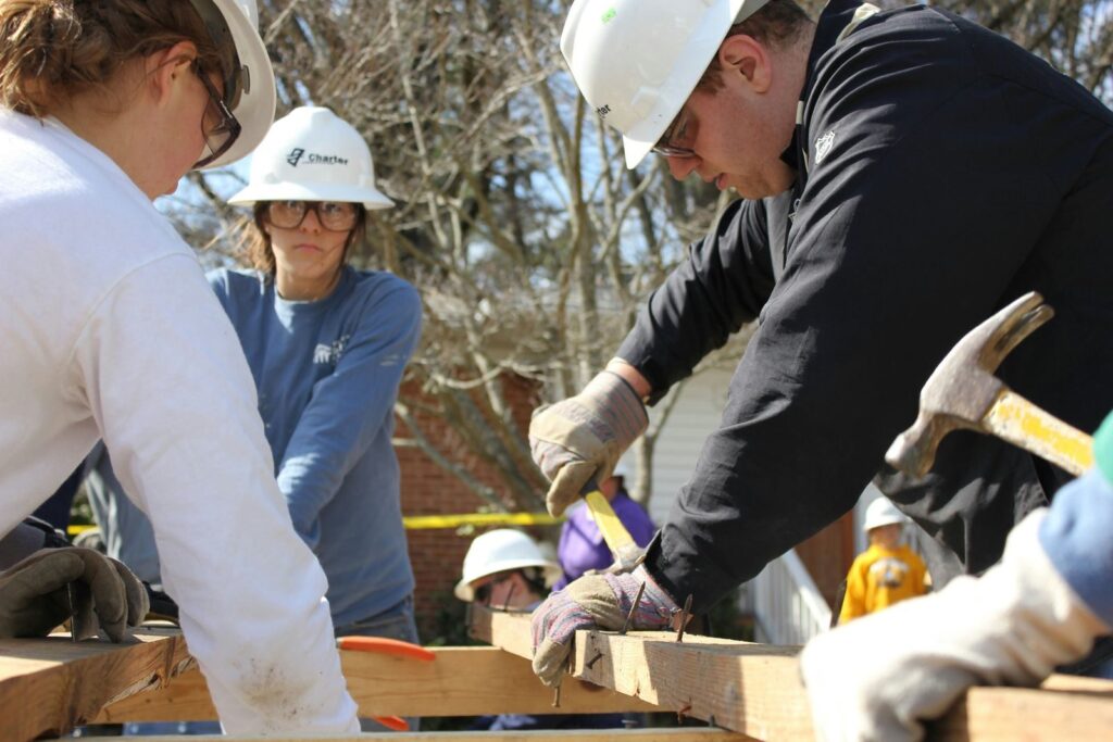 Volunteers work together building a house frame