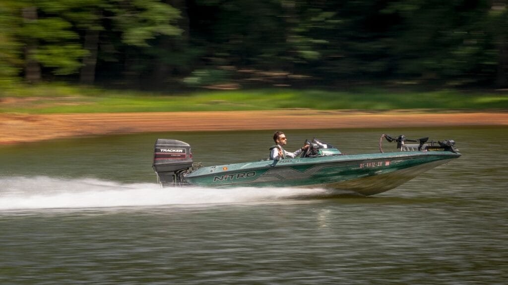 A man driving a fast motorboat on a serene lake surrounded by greenery.