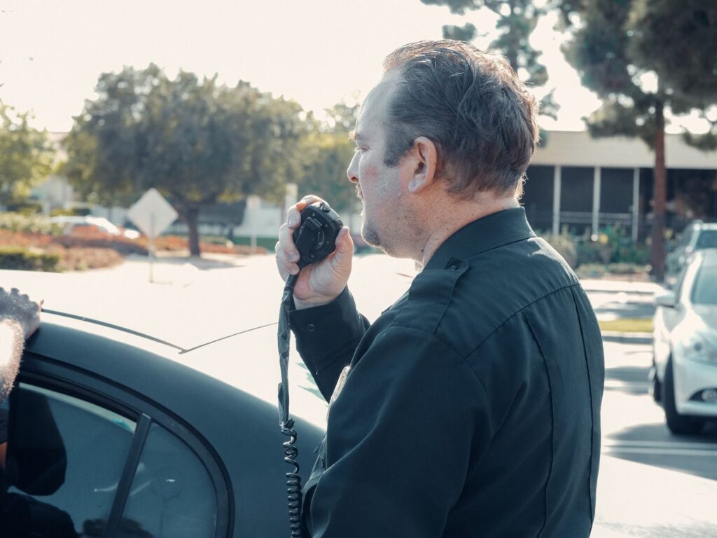 A police officer communicates using a radio outdoors during daytime patrol.