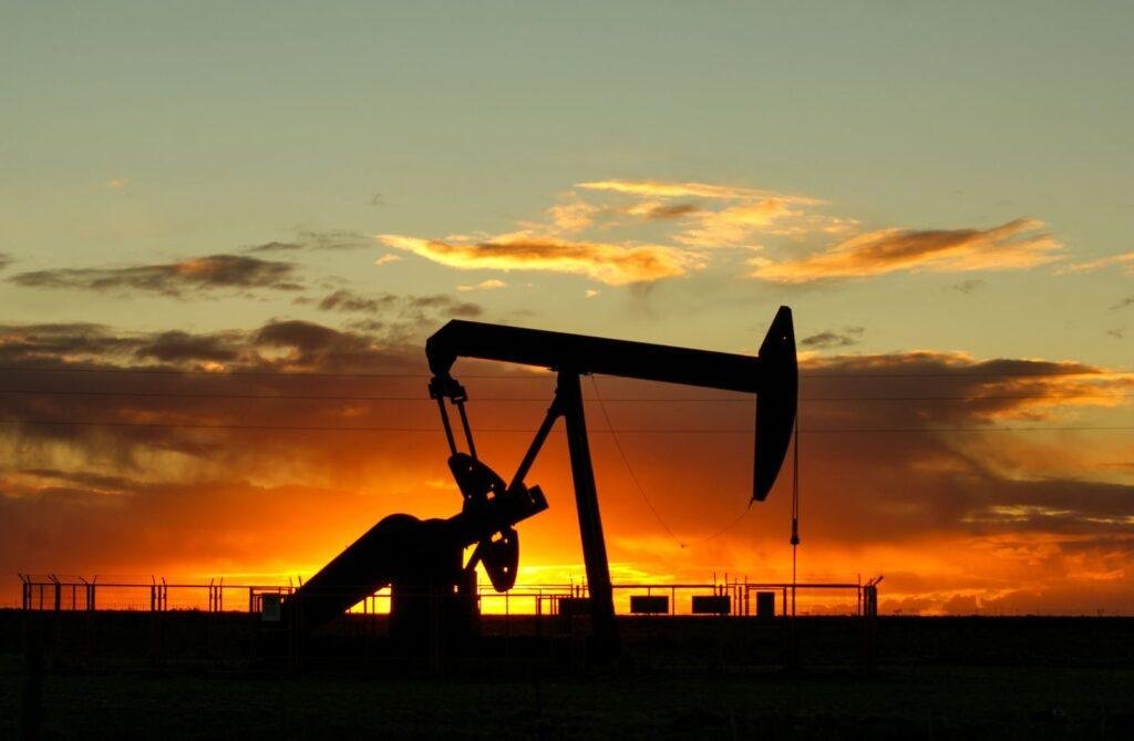 Dramatic silhouette of an oil pump jack against a vibrant sunset sky, emphasizing energy extraction.