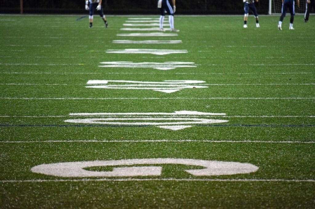 Green football field with white yard line markings under stadium lights