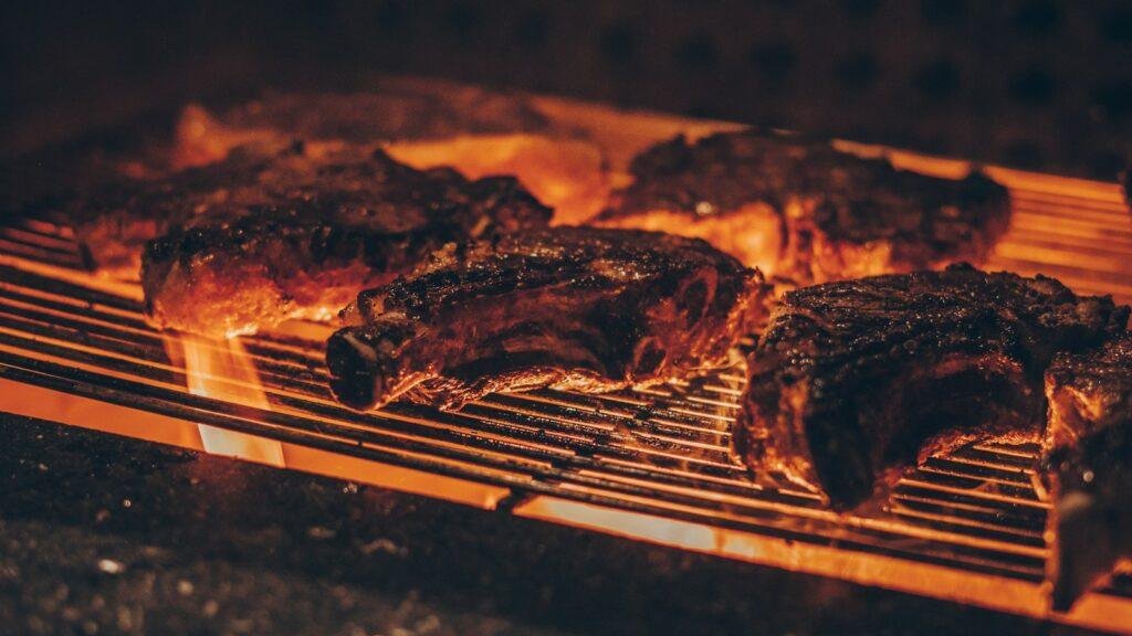 Cuts of meat cooking on an outdoor barbecue grill with light smoke
