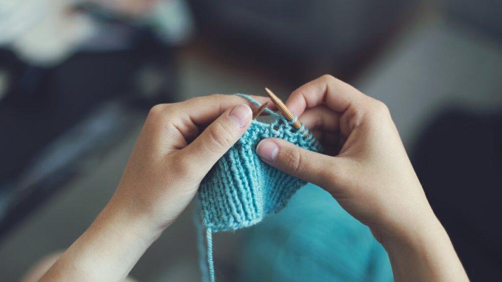 Hands knitting with teal yarn on a pair of needles