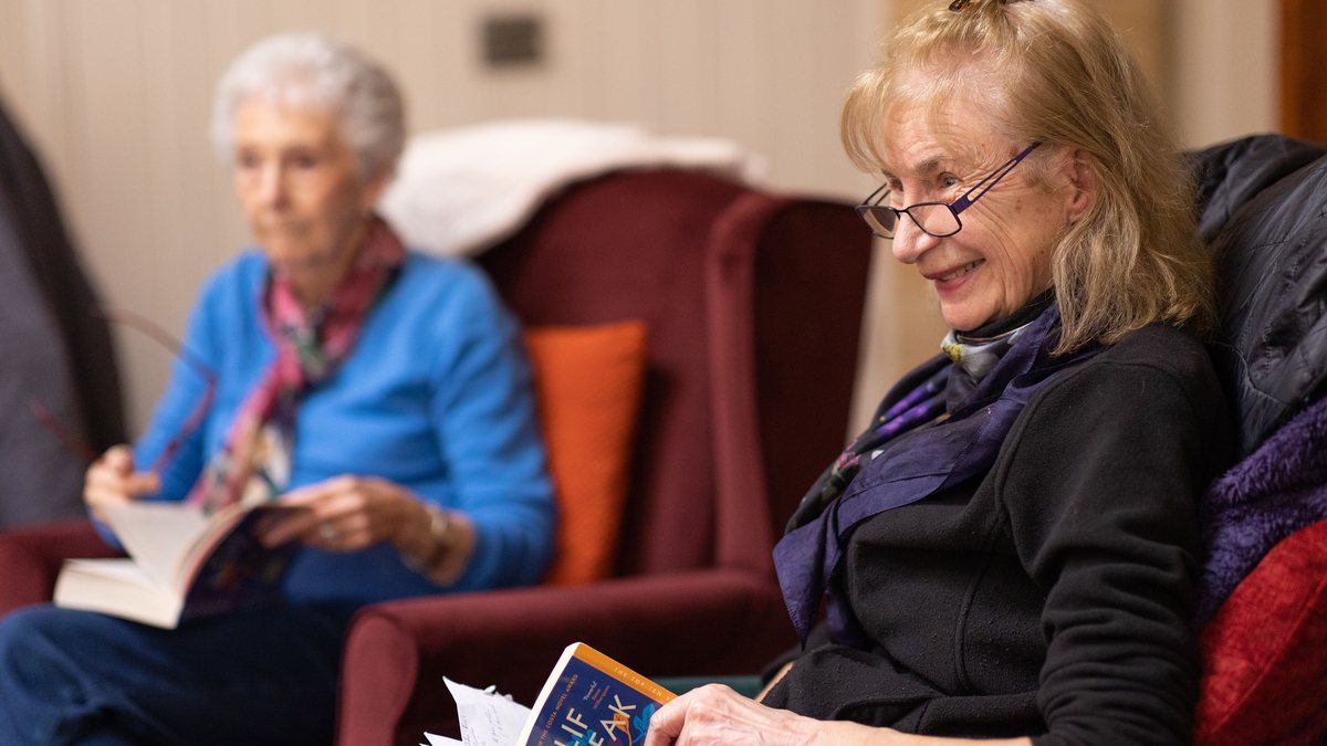Two older women reading books in armchairs