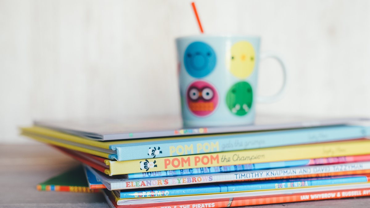 Stack of colorful children's picture books with a mug resting on top