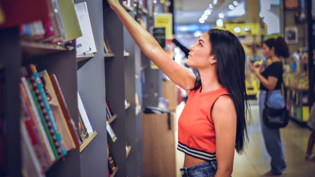 A teenager reaching for a book on a library shelf