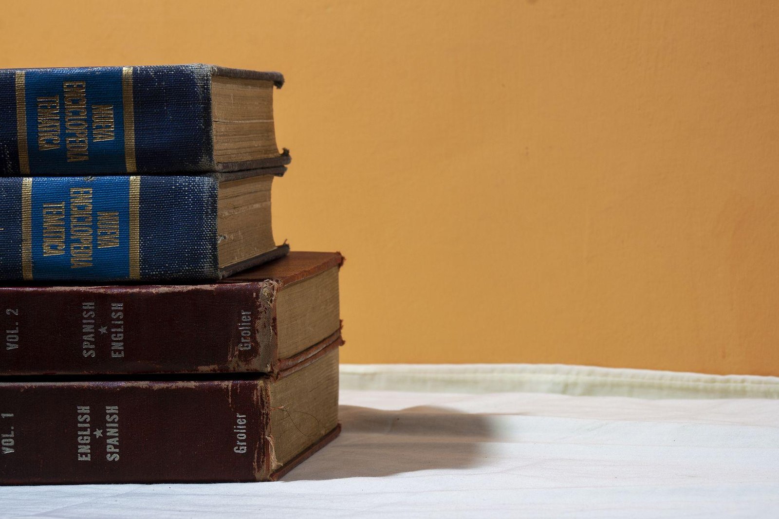 Stack of old English-Spanish dictionaries on a table against a warm wall