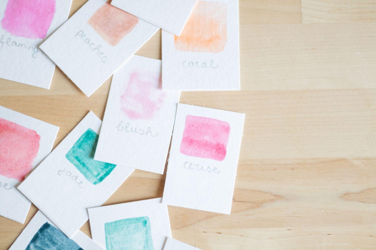 Small hand-painted watercolor cards spread across a light wooden table