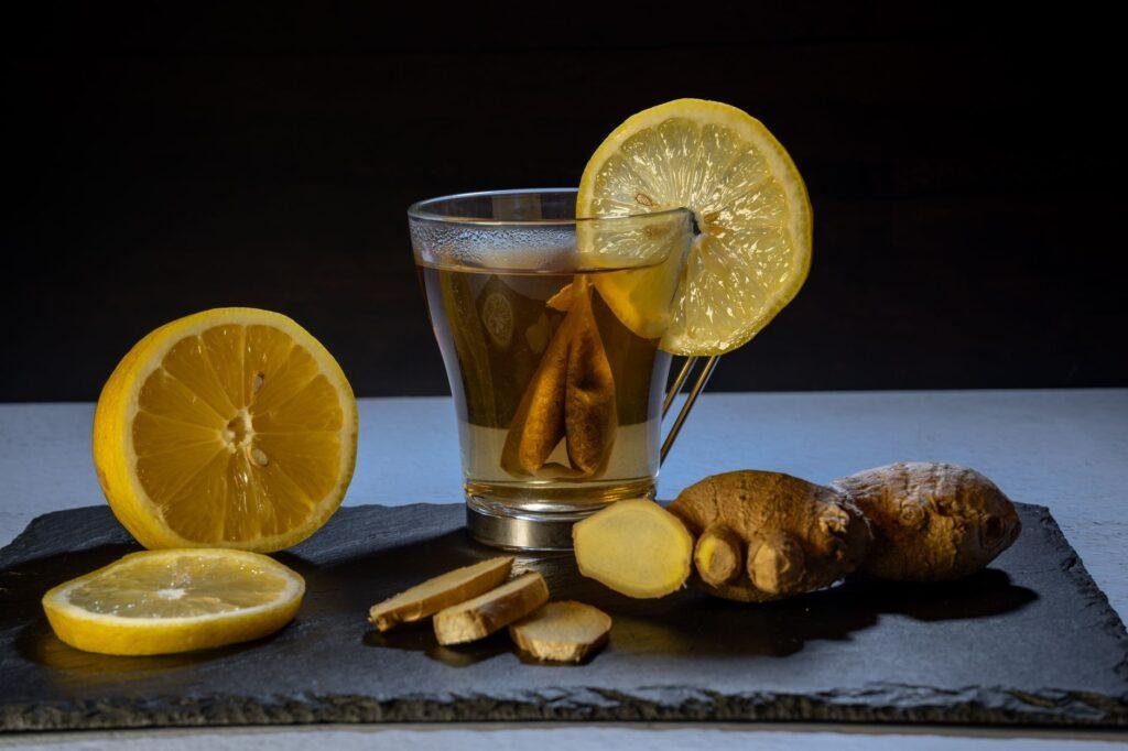 Glass of ginger lemon tea with lemon slices and fresh ginger root on slate