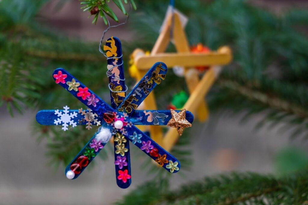 Handmade popsicle stick star ornaments hanging on a pine branch