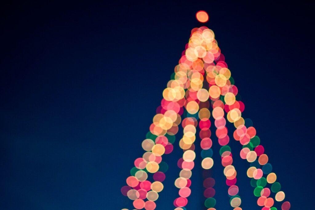 Blurred colorful lights forming the shape of a Christmas tree against a dark blue night sky