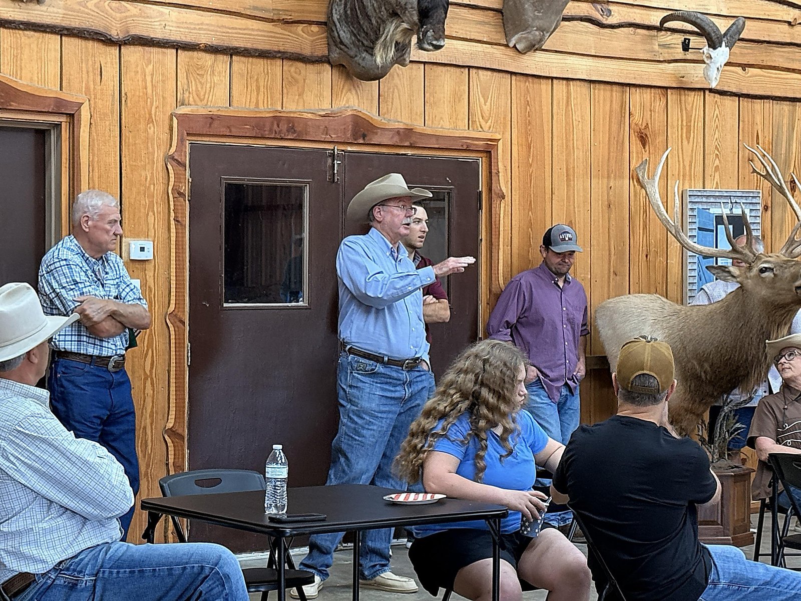 Billy Wayne Cox, in a cowboy hat, gestures as he asks a question in front of wooden double doors.