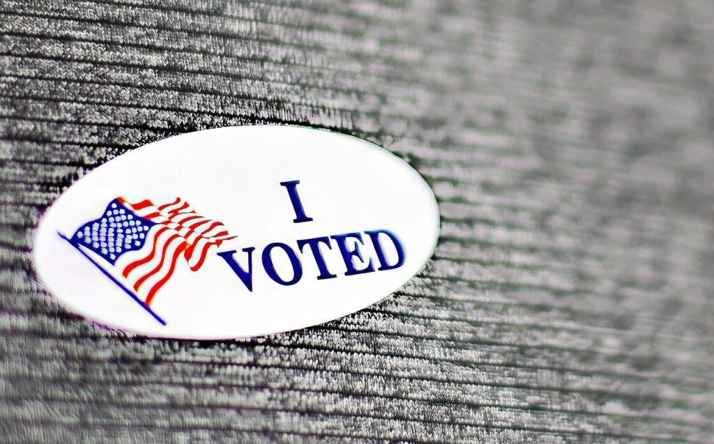 An I Voted sticker with an American flag on a gray fabric background