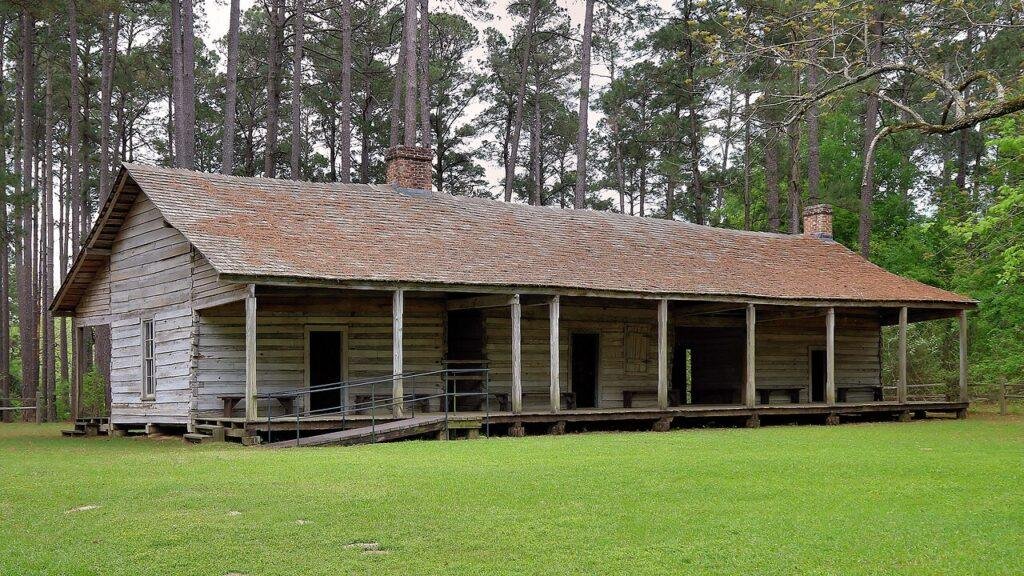 Long weathered log cabin with a wide front porch among tall pines