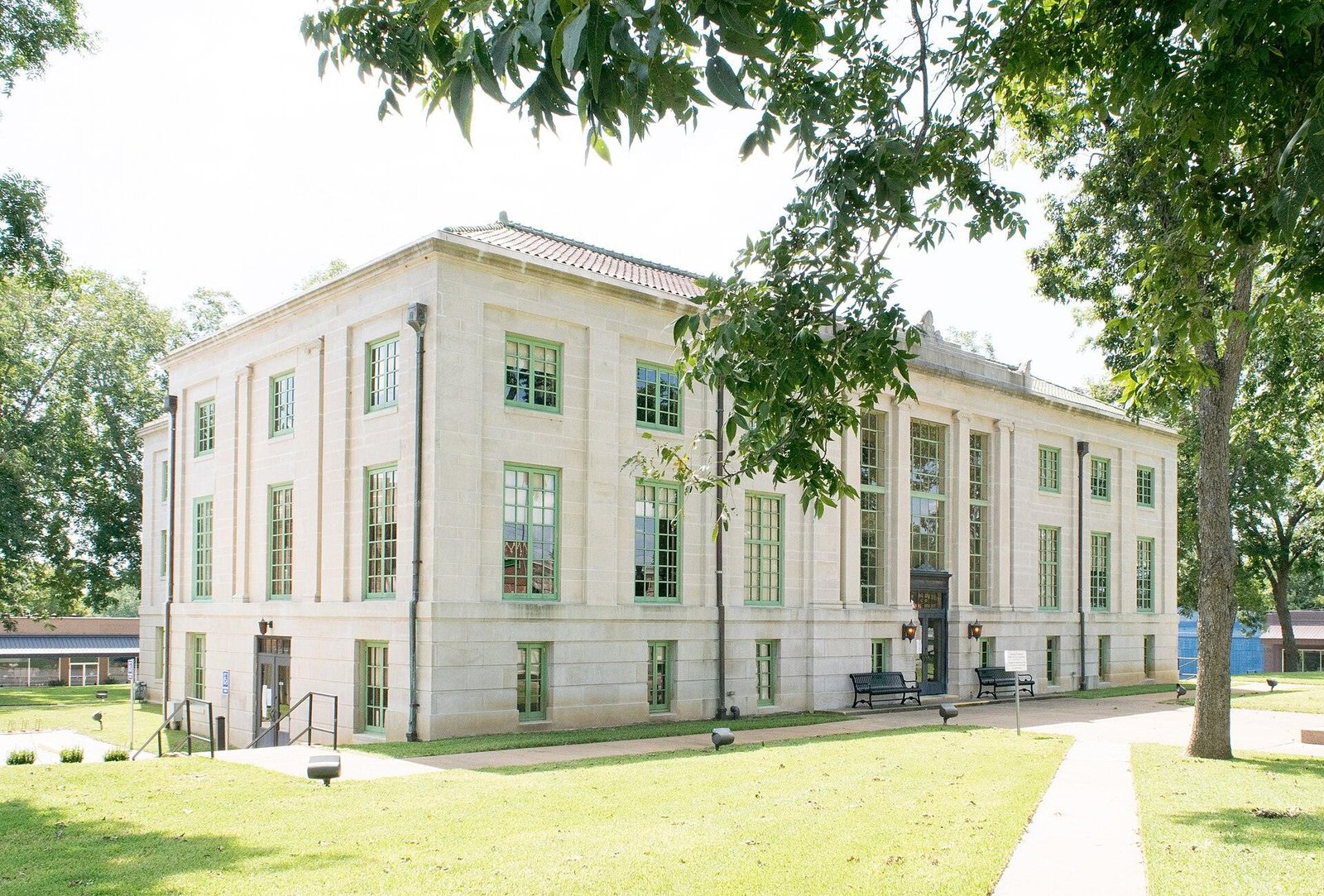 Cream stone county courthouse behind green lawn and shade trees on a sunny day